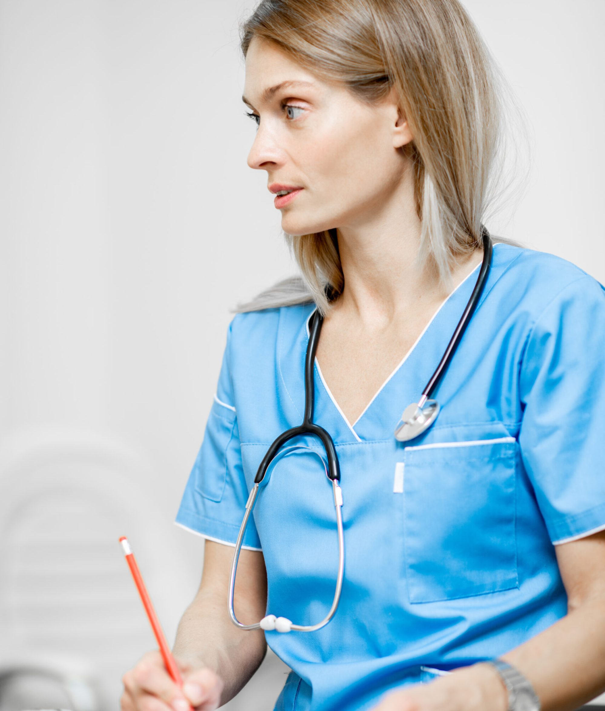 Portrait of a beautiful nurse in blue uniform with stethoscope writing medical history or recipe in the clinic